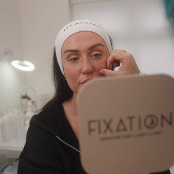 Woman applying makeup with a mirror and 'FIXATION' branding in the background